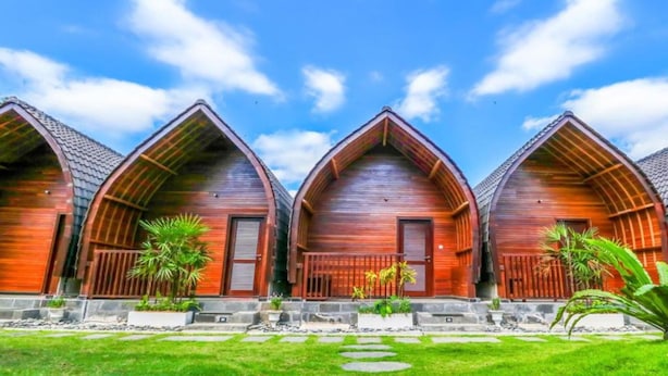 A row of wooden cabins with pitched roofs, arranged in a line with a grassy lawn and potted plants in front.