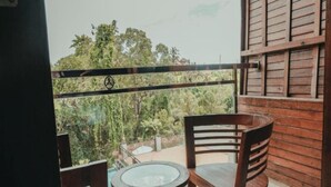 A balcony with wooden chairs and a glass table, overlooking a lush green landscape.