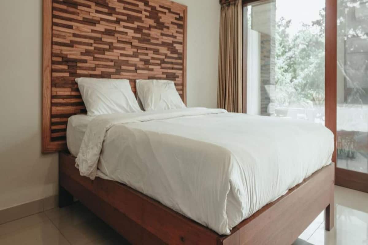 Un dormitorio con cabecera de madera, un ventanal con cortinas y una cama con ropa blanca.