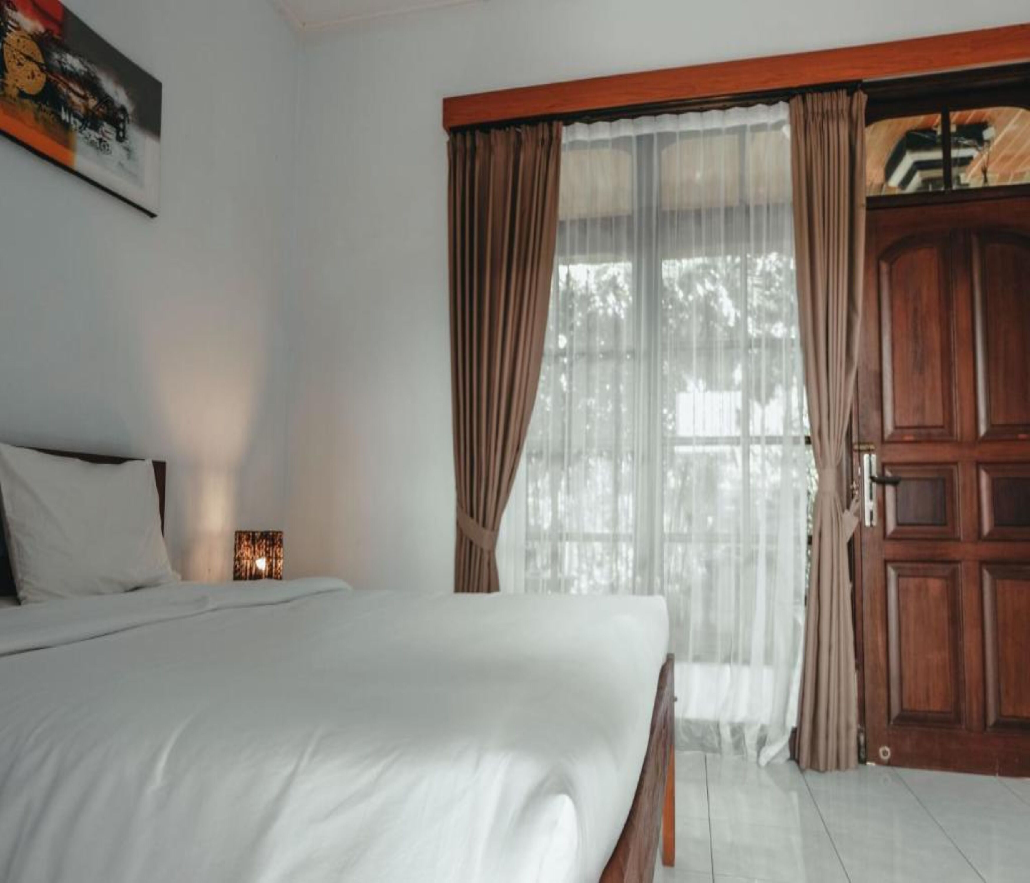 A bedroom with a bed, a nightstand, a wooden door, and a window with curtains.