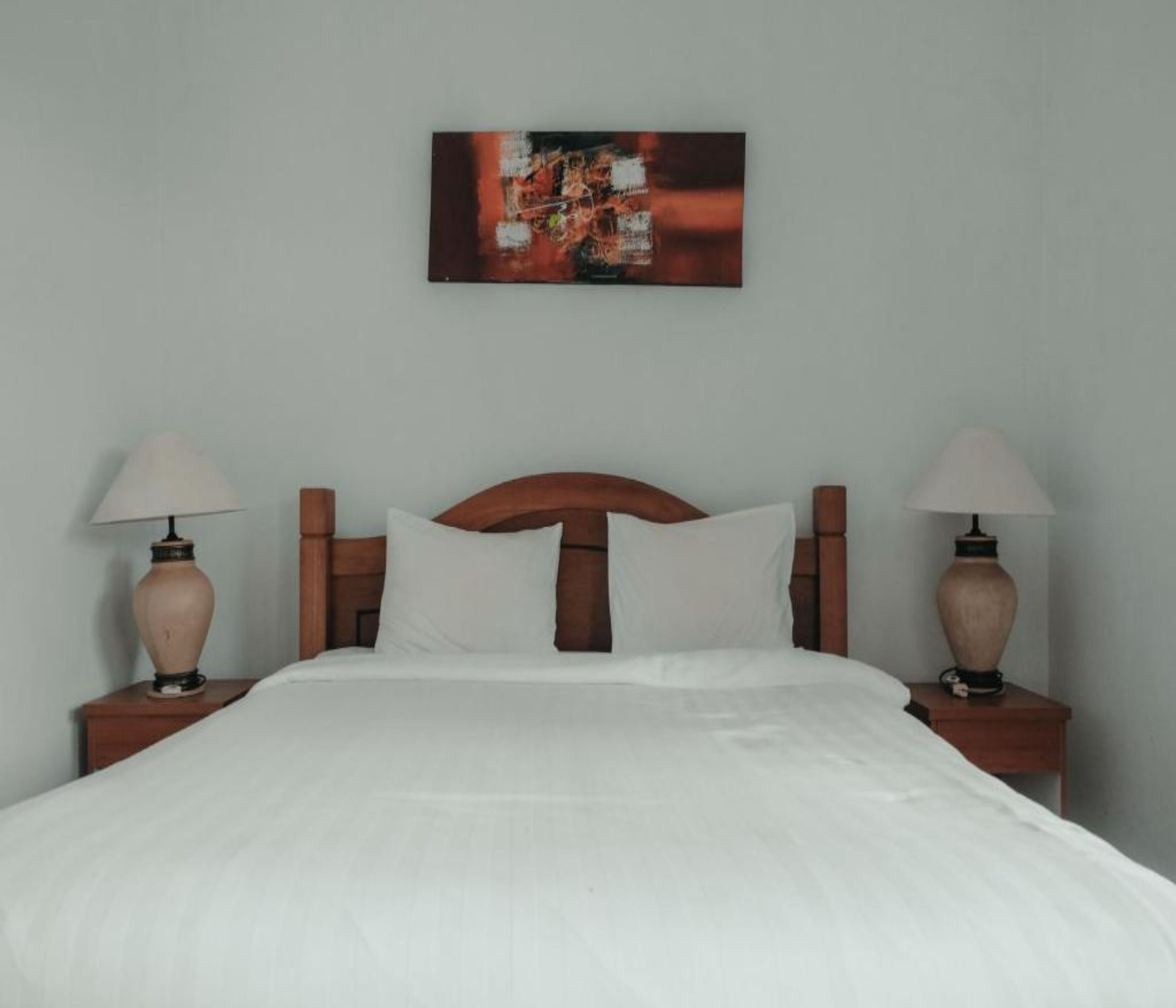 Una cama bien hecha con sábanas blancas, cabecera de madera y dos lámparas de noche sobre mesitas de madera.