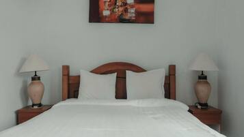 Una cama bien hecha con sábanas blancas, cabecera de madera y dos lámparas de noche sobre mesitas de madera.