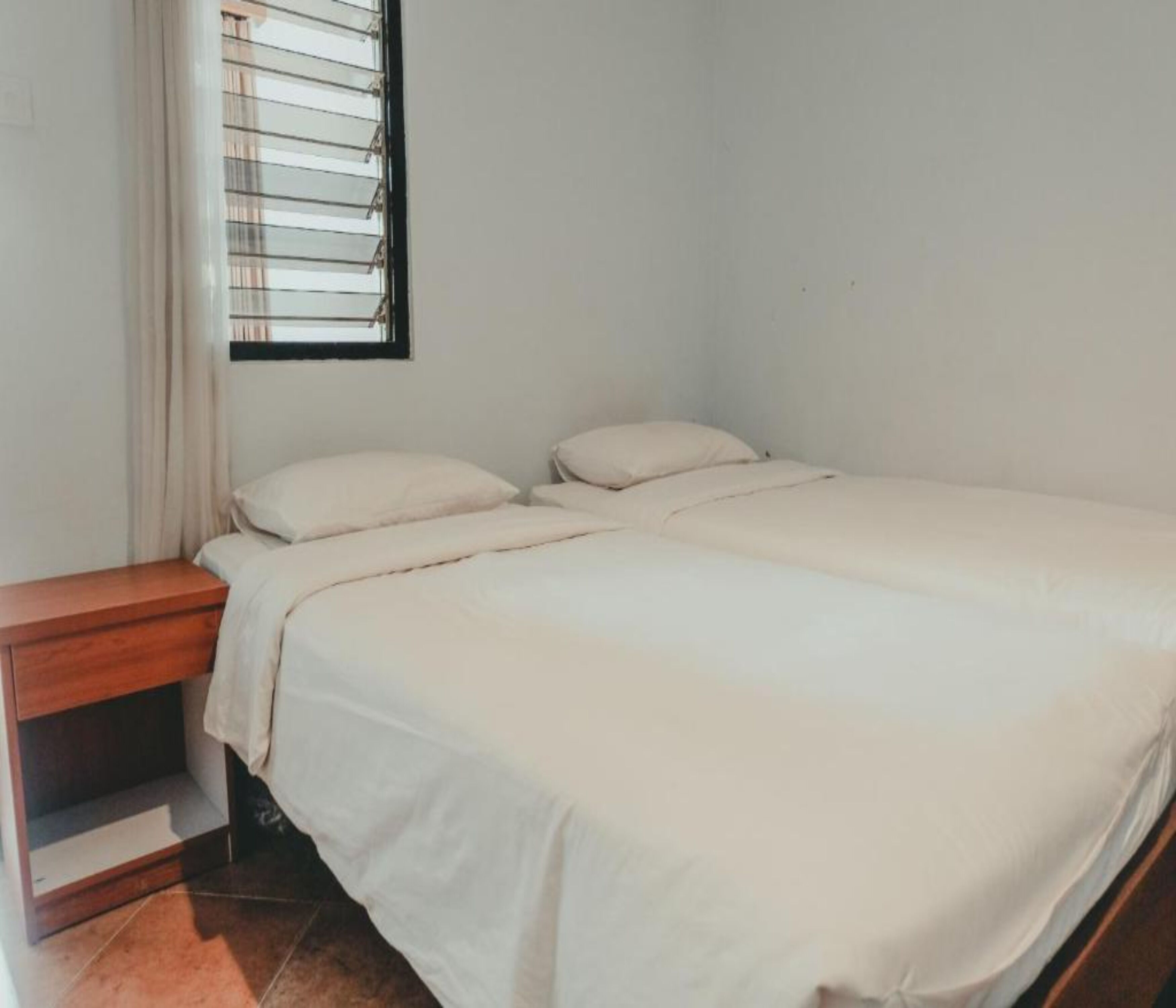 A simple, clean room with a bed, a nightstand, and a window with blinds.