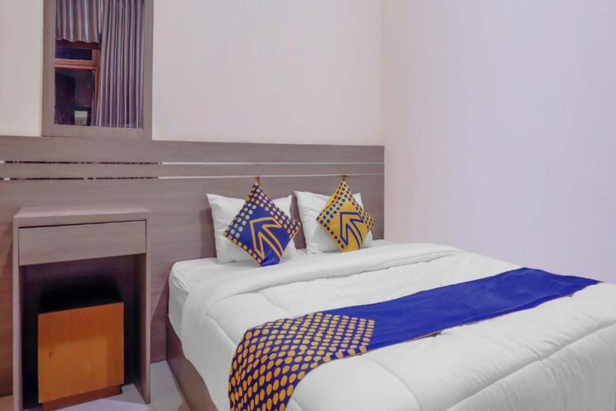 Habitació d'hotel amb llit, una vetust i un mirall, i una finestra amb cortines.
