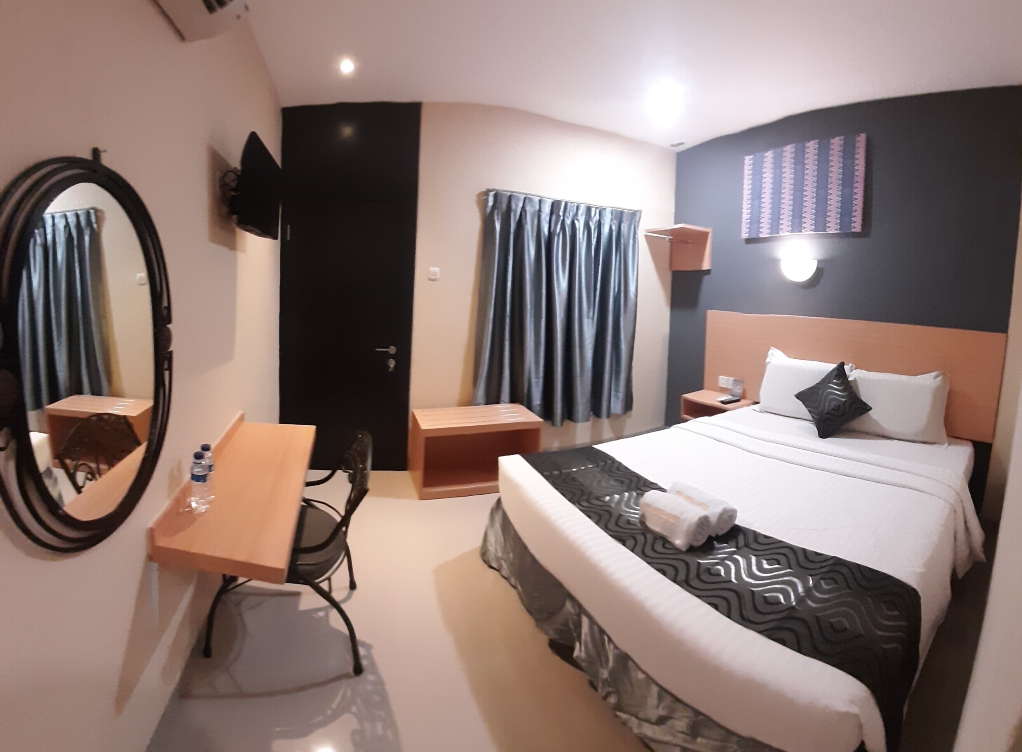 Une chambre d’hôtel avec un lit, un bureau, une chaise, un miroir, une télévision et une porte.