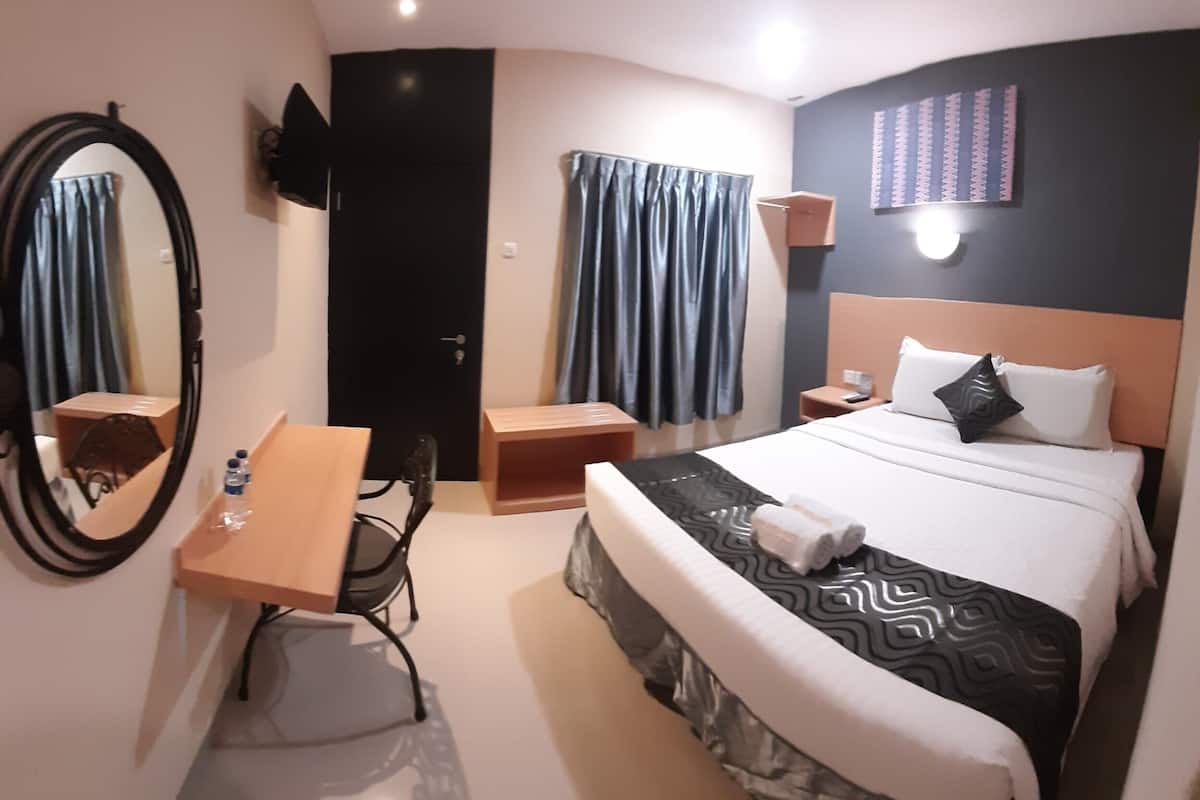 Hotellihuone, jossa on sänky, työpöytä, tuoli, peili, televisio ja ovi.