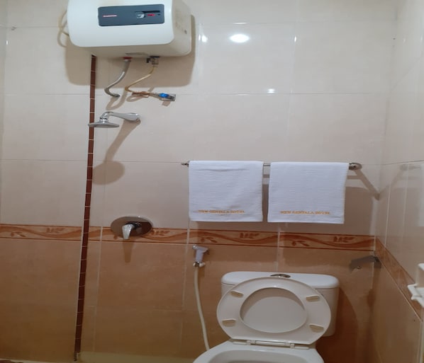 Um banheiro com vaso sanitário, chuveiro e secador de mãos. Há duas toalhas penduradas em um suporte com a inscrição "NEW GENTALA HOTEL".