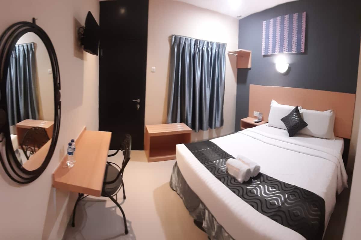 Hotellihuone, jossa on sänky, työpöytä, tuoli, peili, vaatekaappi ja seinälle asennettu televisio.