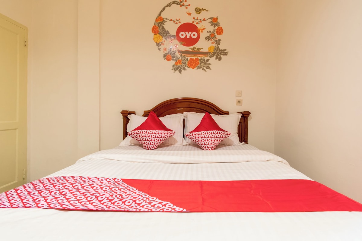 Una cama con ropa blanca y almohadas con estampado rojo y blanco, además de una manta con diseño rojo y blanco, y una decoración de pared con la palabra "OYO".