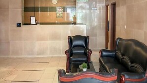 A reception area with a counter, two leather chairs, a small table with a plant, and a clock on the wall. - New Hotel Gentala (Medan)