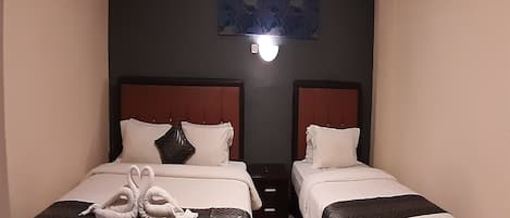 A hotel room with two beds, a nightstand, an air conditioning unit, and a wall-mounted light fixture.