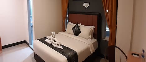 A hotel room with a bed, a chair, a table, an air conditioning unit, and a window with curtains.