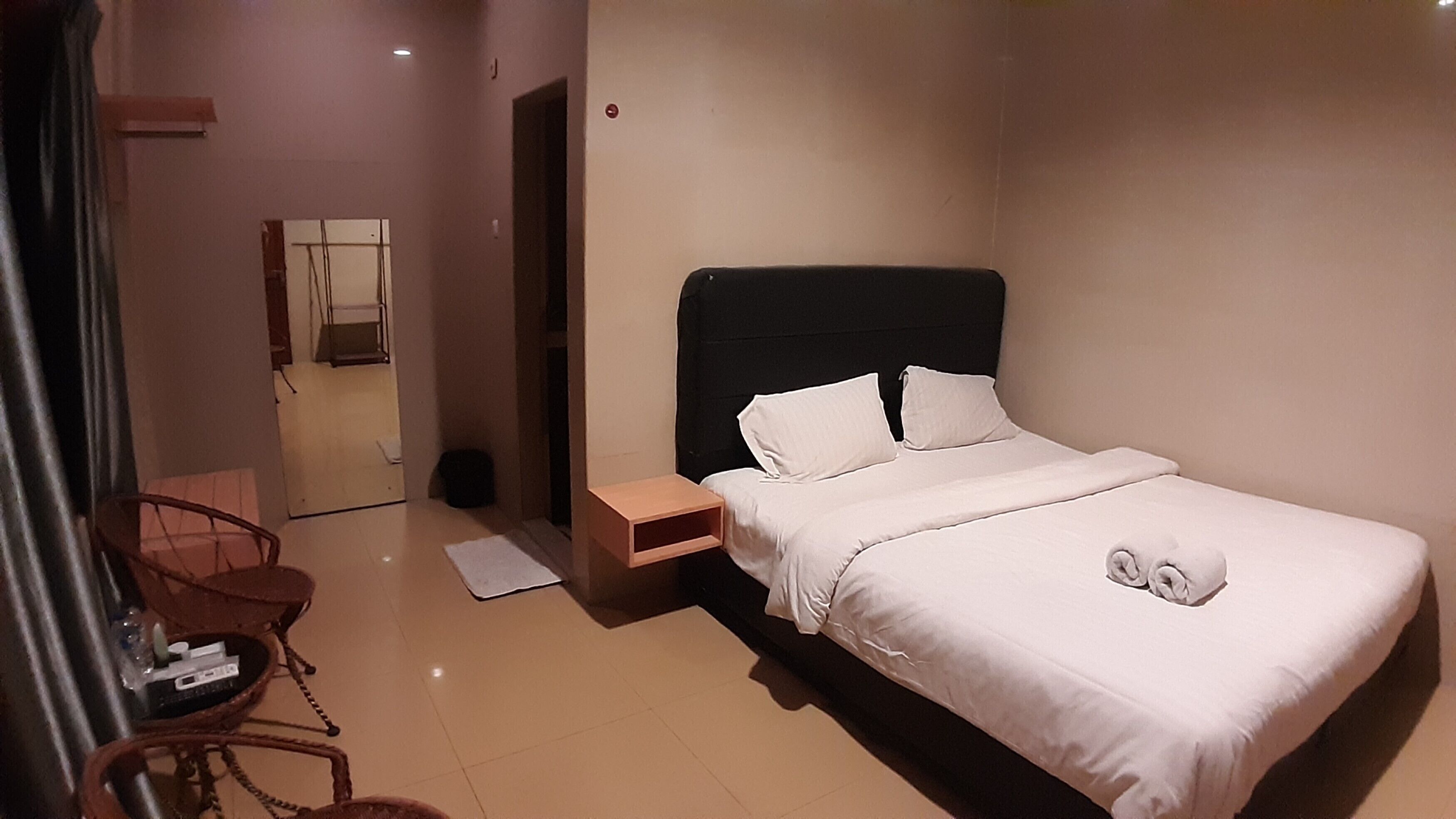 Une chambre d’hôtel bien rangée, avec un lit simple, une table de chevet, une chaise et une petite table sur laquelle se trouvent une bouteille et une télécommande.