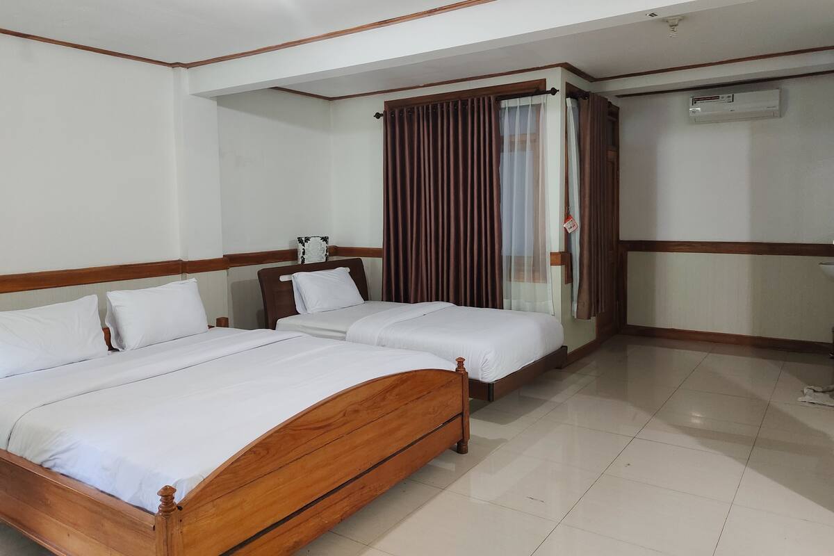 A hotel room with two wooden beds, white bedding, a wooden headboard, a window with curtains, and a ceiling fan.