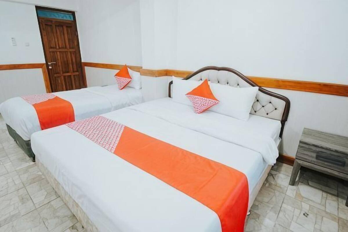 A hotel room with two beds, a wooden door, and a small wooden bench.