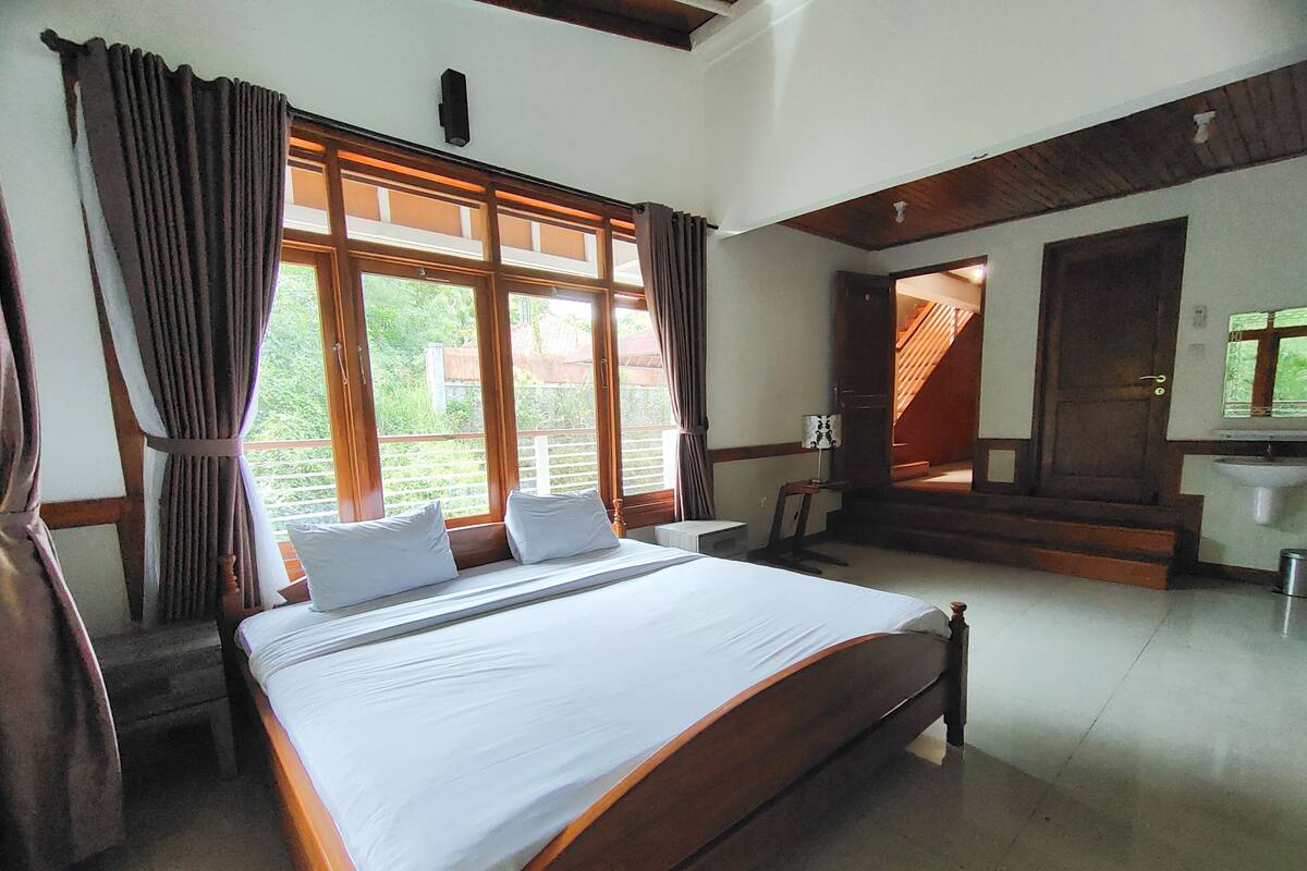 A spacious bedroom with a large bed, wooden headboard, and a view of the outdoors through large windows.