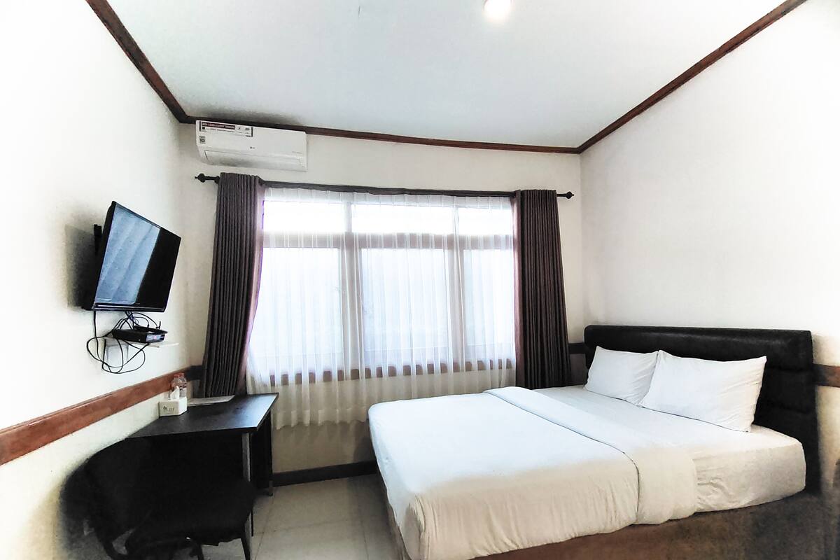 A hotel room with a bed, a desk with a TV, and a window with curtains.