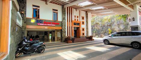 A guesthouse with a stone facade, a signboard, a motorcycle parked outside, and a car parked in front.