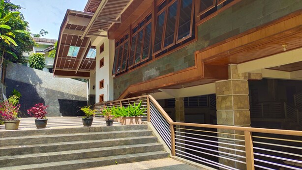 Un edificio con una escalera que lleva a un segundo piso, muros de piedra y plantas en macetas.