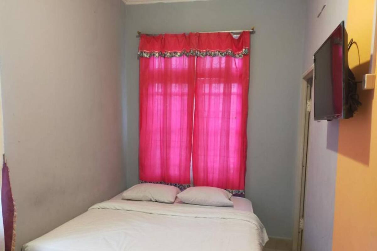 A bedroom with a bed, pink curtains, and a television on the wall.