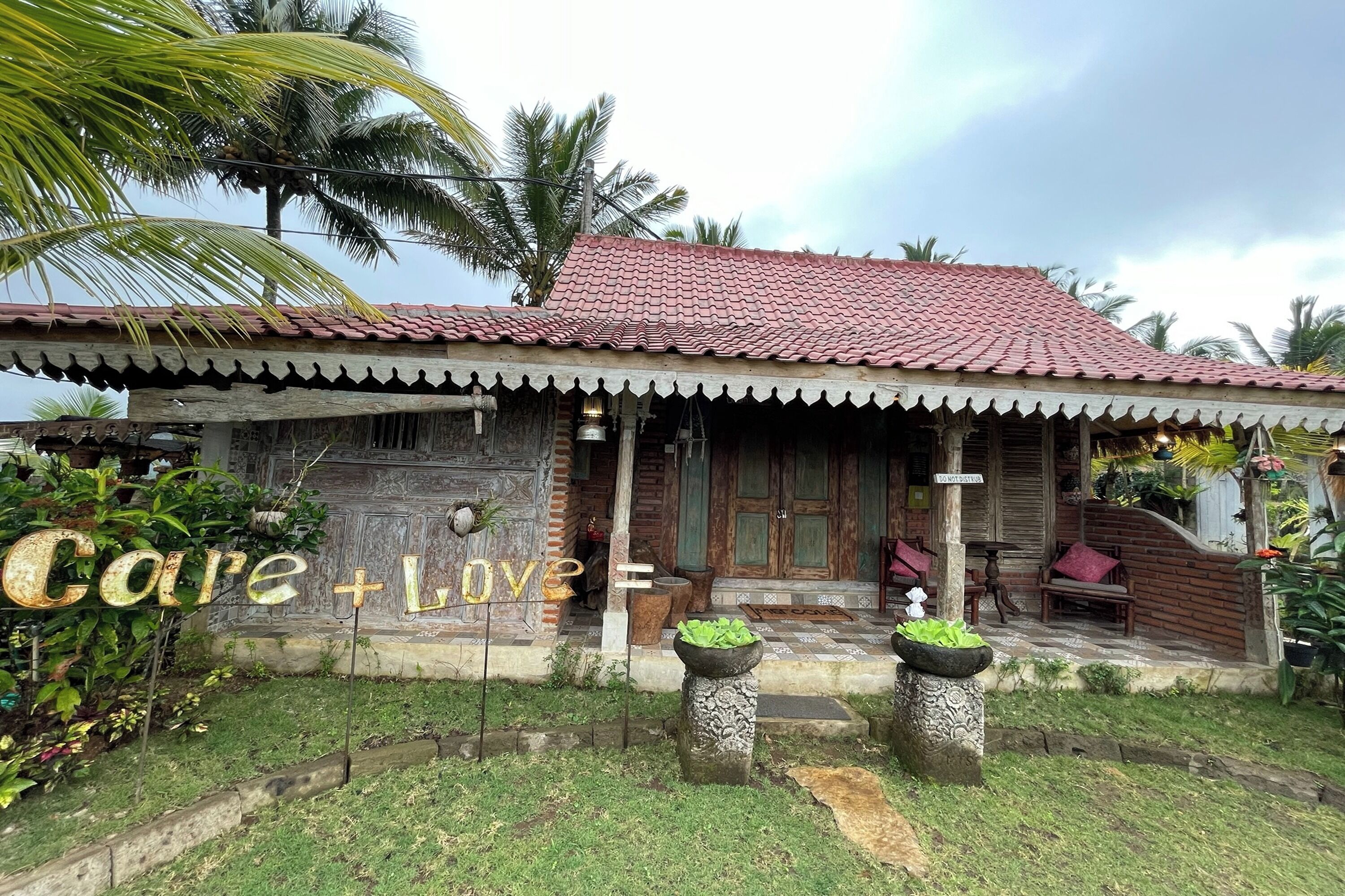 A traditional house with a tiled roof, a porch with wooden furniture, and a sign reading "Care + Love".
