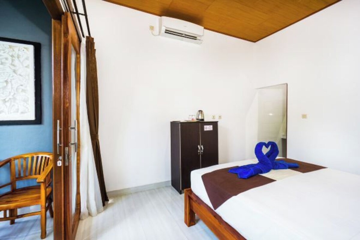 A hotel room with a bed, a wooden chair, a wardrobe, and a mirror.