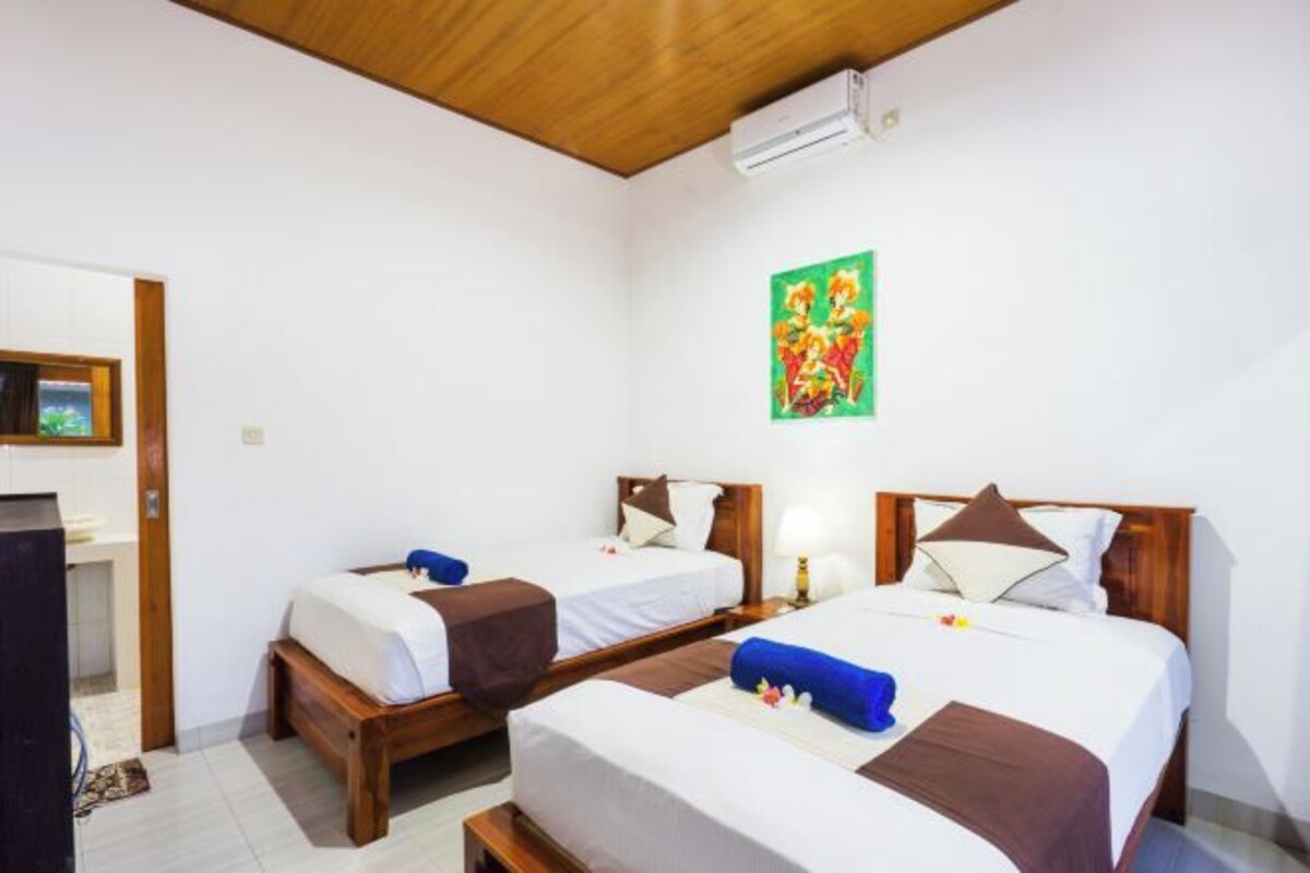 A hotel room with two single beds, a wooden ceiling, a wall-mounted air conditioner, and a painting.