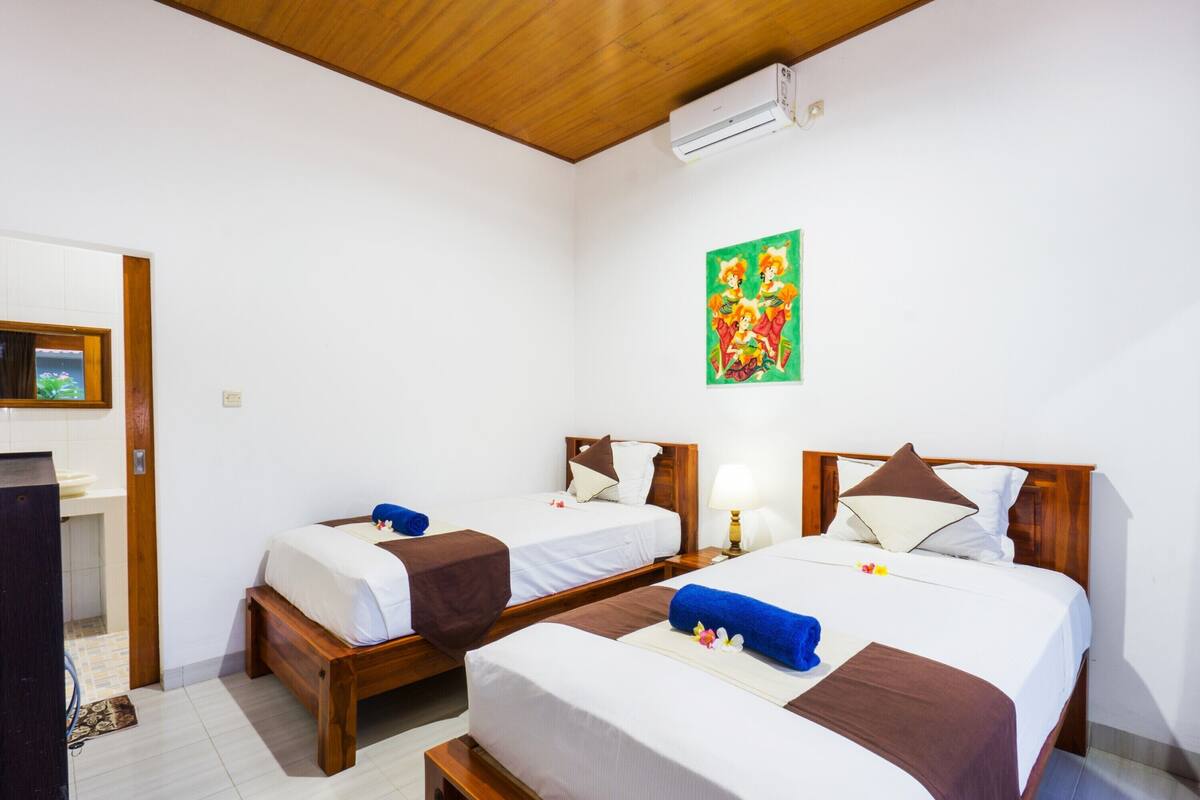Une chambre d’hôtel avec deux lits, un plafond en bois, un climatiseur et un tableau coloré au mur.