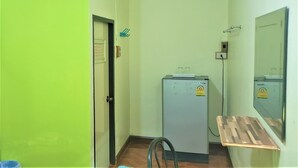 A compact room with a door, a small refrigerator, a mirror, and a wooden shelf. - Pattaraporn Hotel (Pranburi)