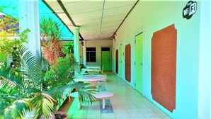 A corridor with green doors, potted plants, and outdoor seating. - Pattaraporn Hotel (Pranburi)