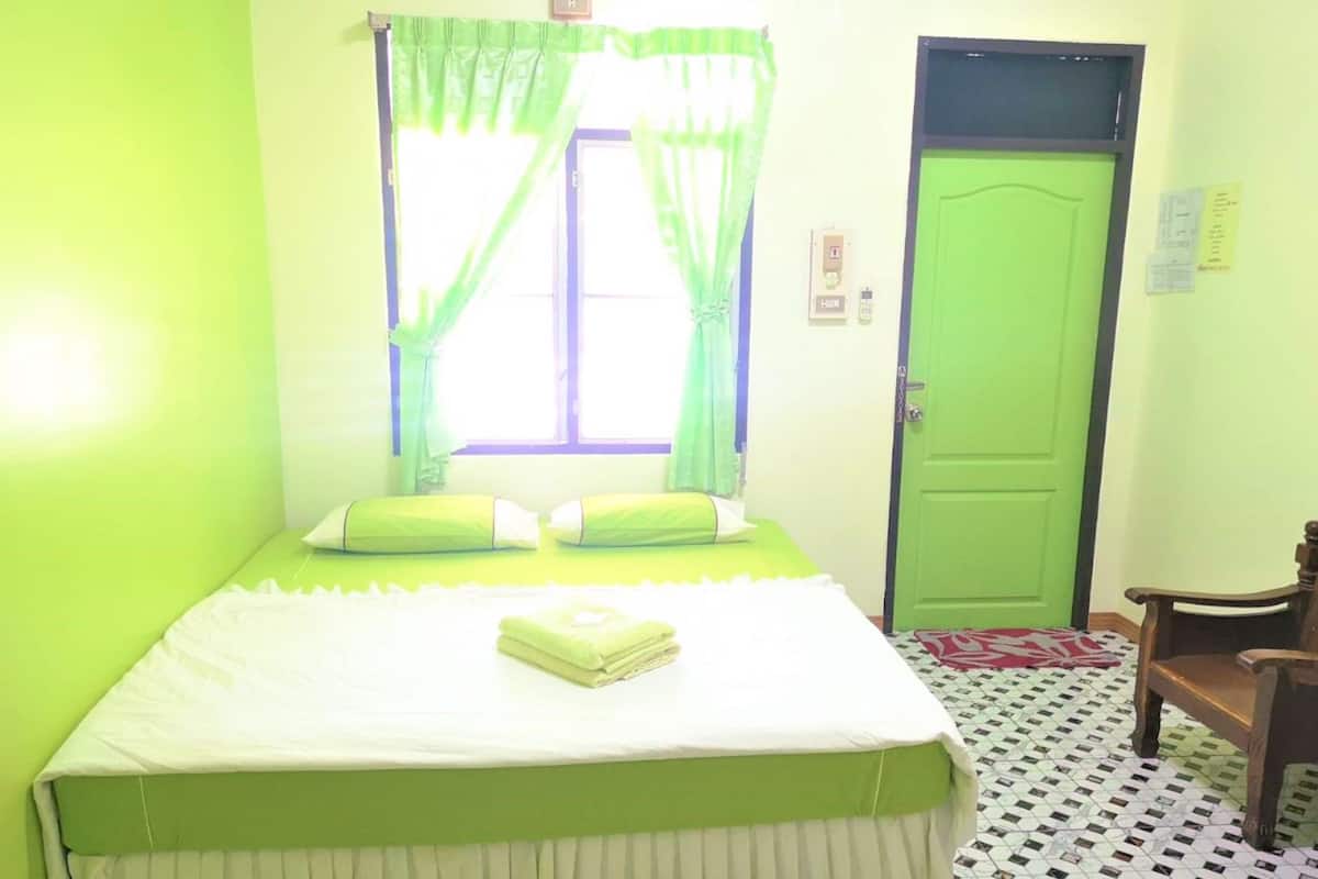A room with a bed, a green door, and a window with green curtains.