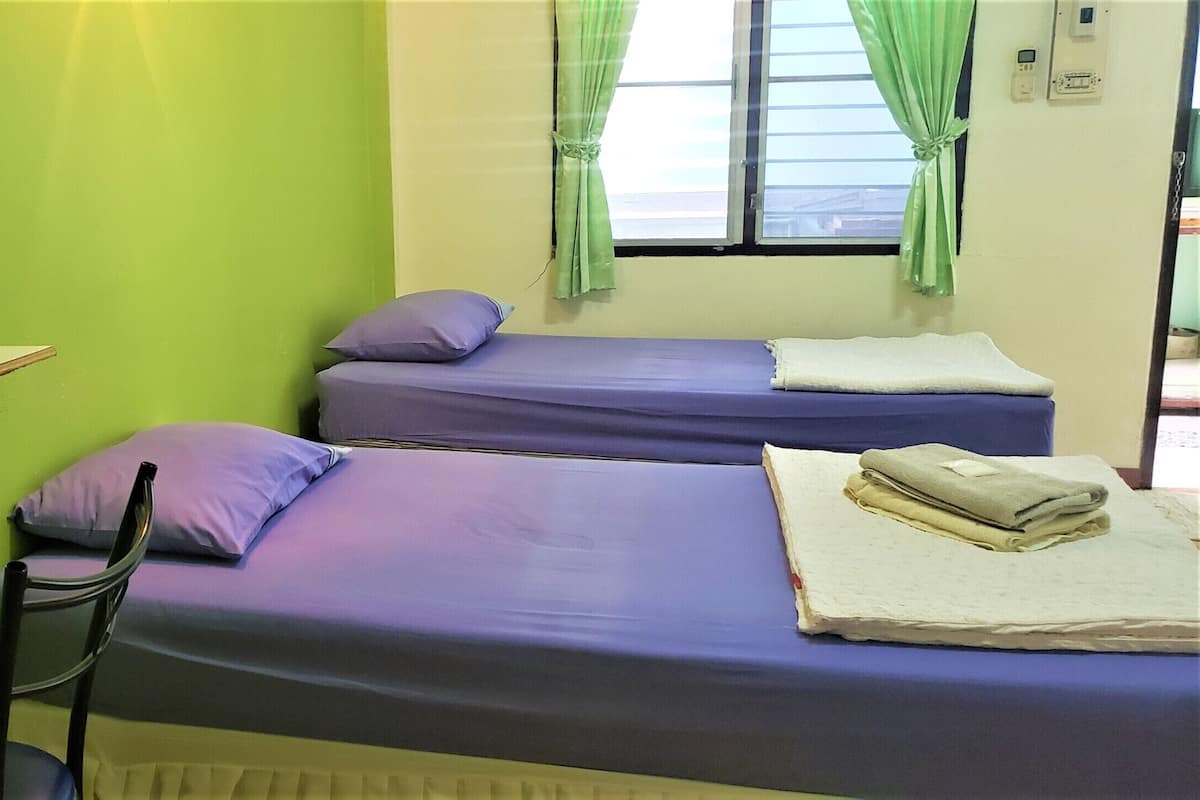 A room with two beds, a chair, a mirror, and a window with curtains.