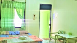 A room with a bed, a table, and a chair. There is a window with curtains, a door, and a wall-mounted television. - Pattaraporn Hotel (Pranburi)