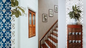 A staircase with wooden steps and metal railings, a wall with framed pictures, and a potted plant on a cabinet. - Baan Chiang Bed Lampang (Lampang)