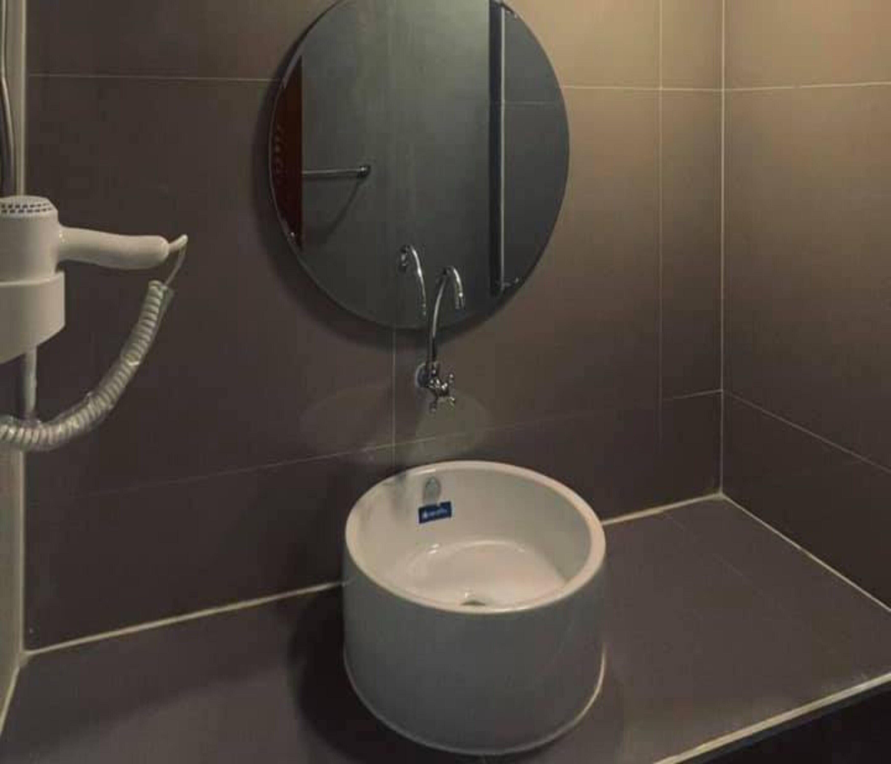 A bathroom with a round sink, a mirror, and a hairdryer.