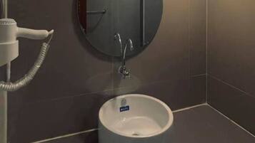 A bathroom with a round sink, a mirror, and a hairdryer.
