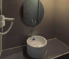 Un baño con un lavamanos redondo, un espejo y un secador de pelo.