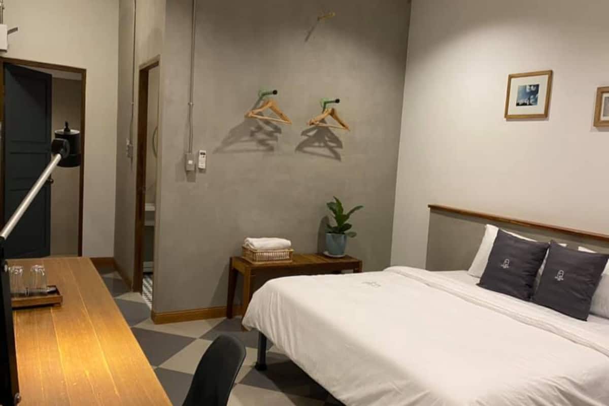 Een hotelkamer met een bed, een bureau, een stoel, een kleine tafel met een plant en een muur met twee ingelijste foto's.