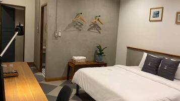 A hotel room with a bed, a desk, a chair, a small table with a plant, and a wall with two framed pictures.