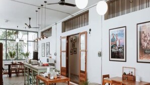 A modern dining area with wooden tables and chairs, a bar area, and framed pictures on the walls. - Baan Chiang Bed Lampang (Lampang)