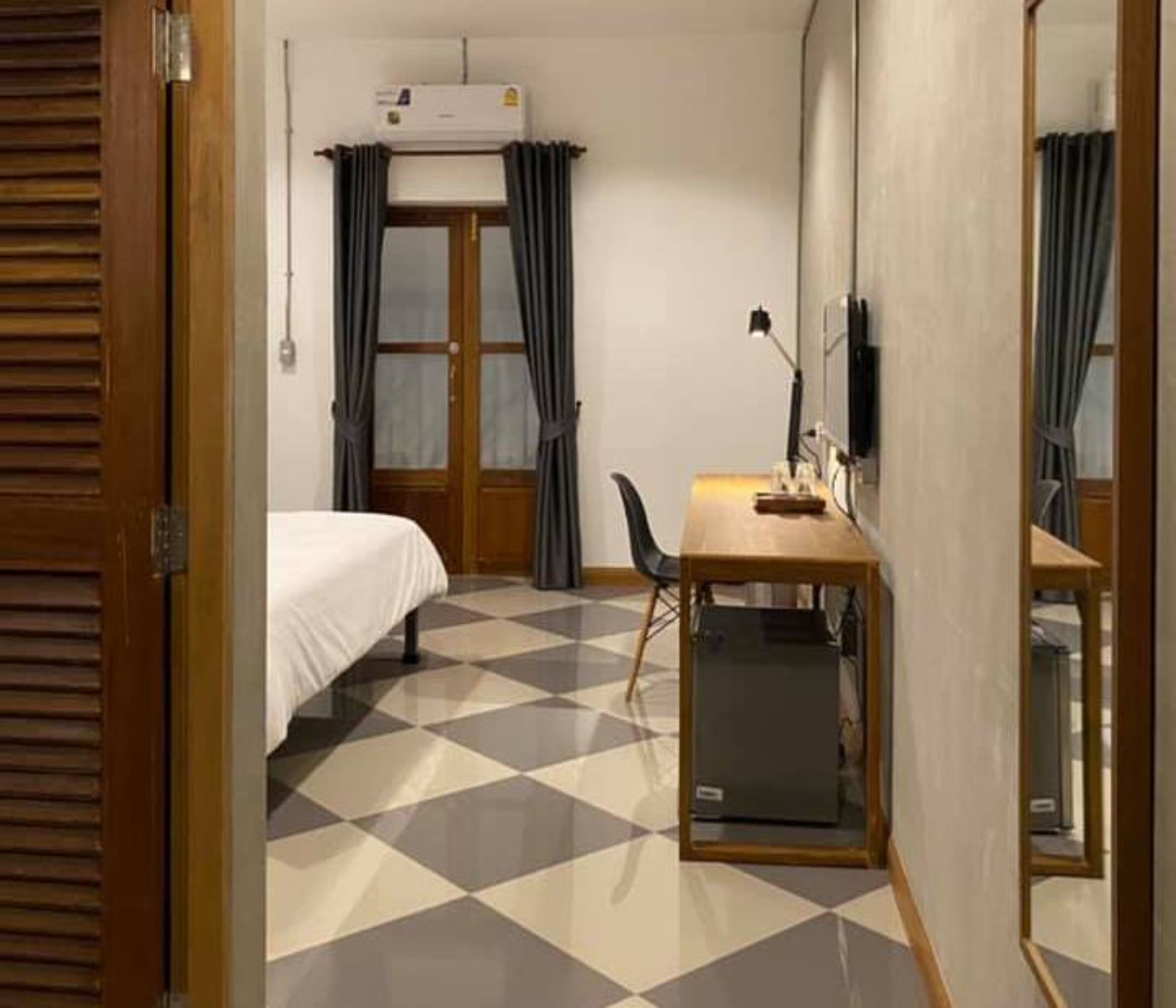 A hotel room with a bed, a desk with a chair, and a large mirror.