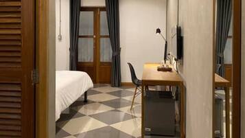 A hotel room with a bed, a desk with a chair, and a large mirror.
