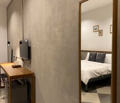 Un dormitorio con una cama, un escritorio con computadora y un televisor en la pared.