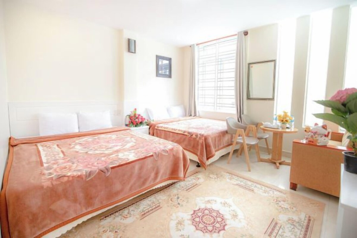 A hotel room with two beds, a desk, a chair, a small table, a mirror, and a window with curtains.