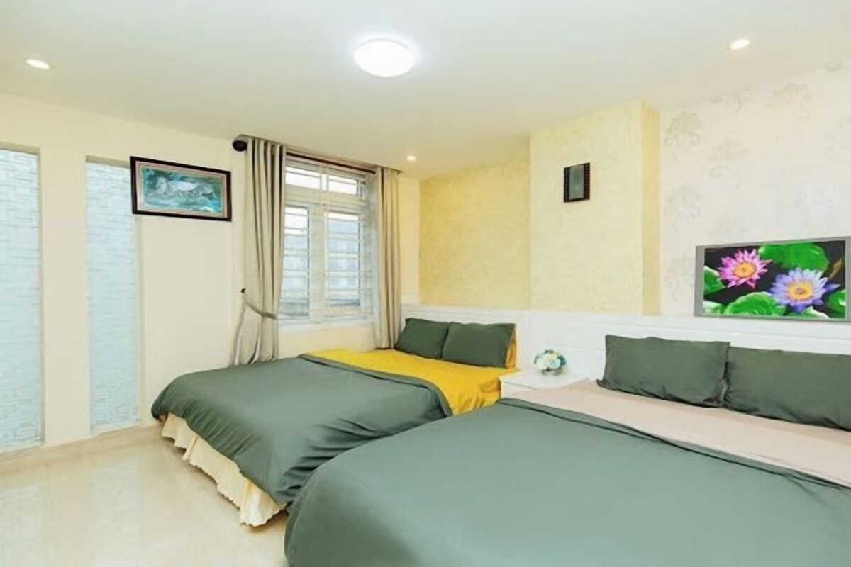 Une chambre d’hôtel avec deux lits, une fenêtre avec des rideaux, un tableau au mur et une petite table sur laquelle se trouve un vase.