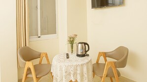Een klein eetgedeelte met twee stoelen, een tafel met kantkleed, een waterkoker en een vaas met bloemen.