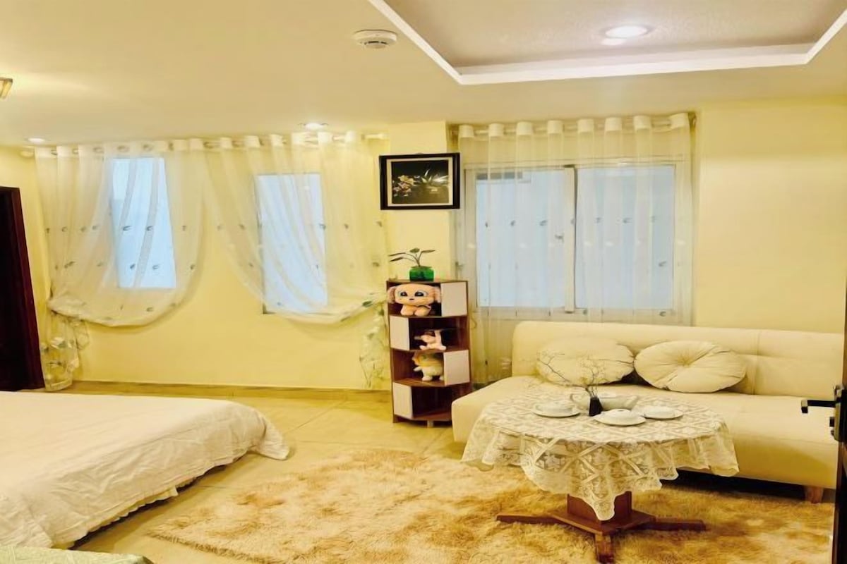 A bedroom with a bed, a sofa, a small table, and a window with curtains.