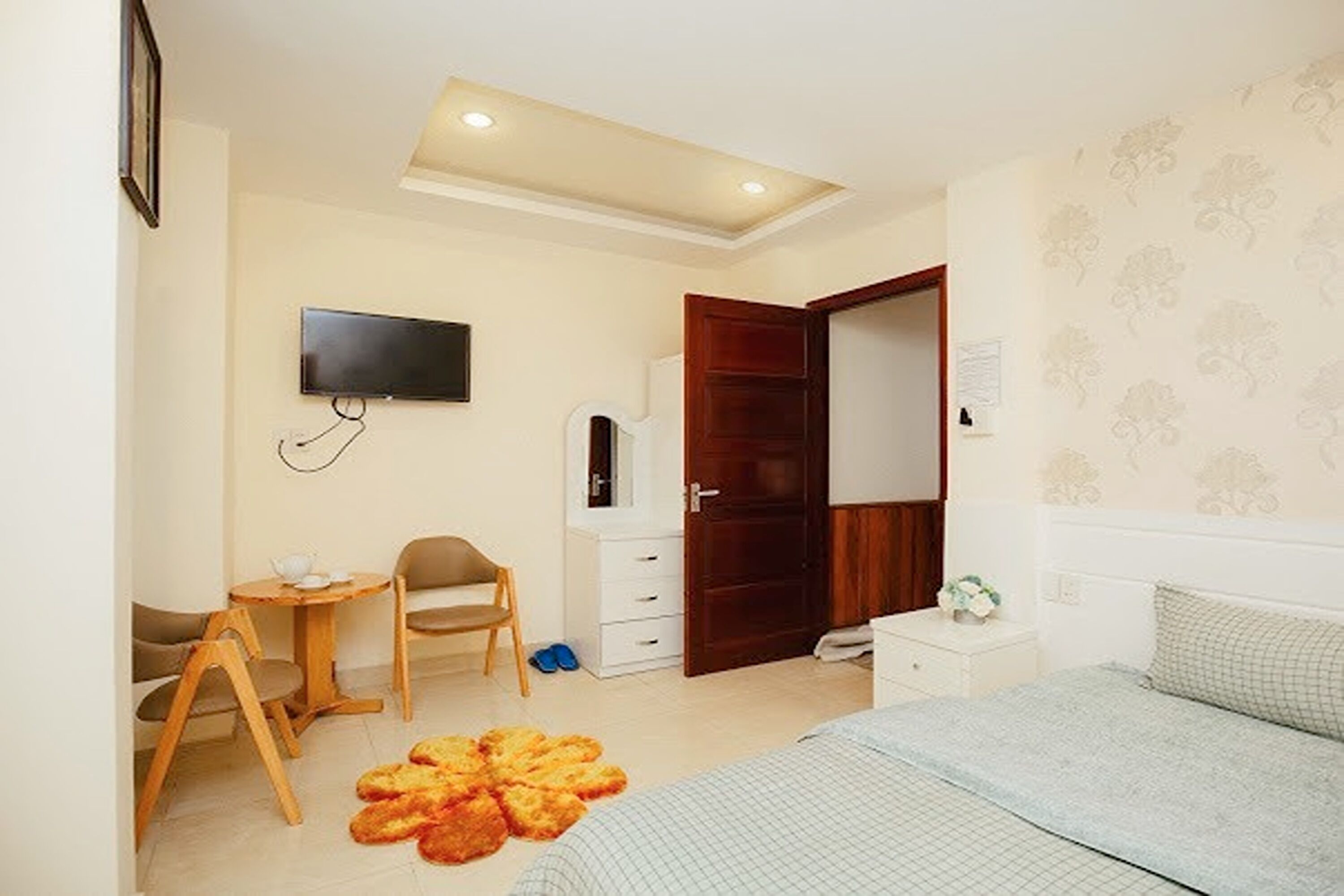 A bedroom with a bed, a desk with a chair, a television, a wardrobe, and a small rug.
