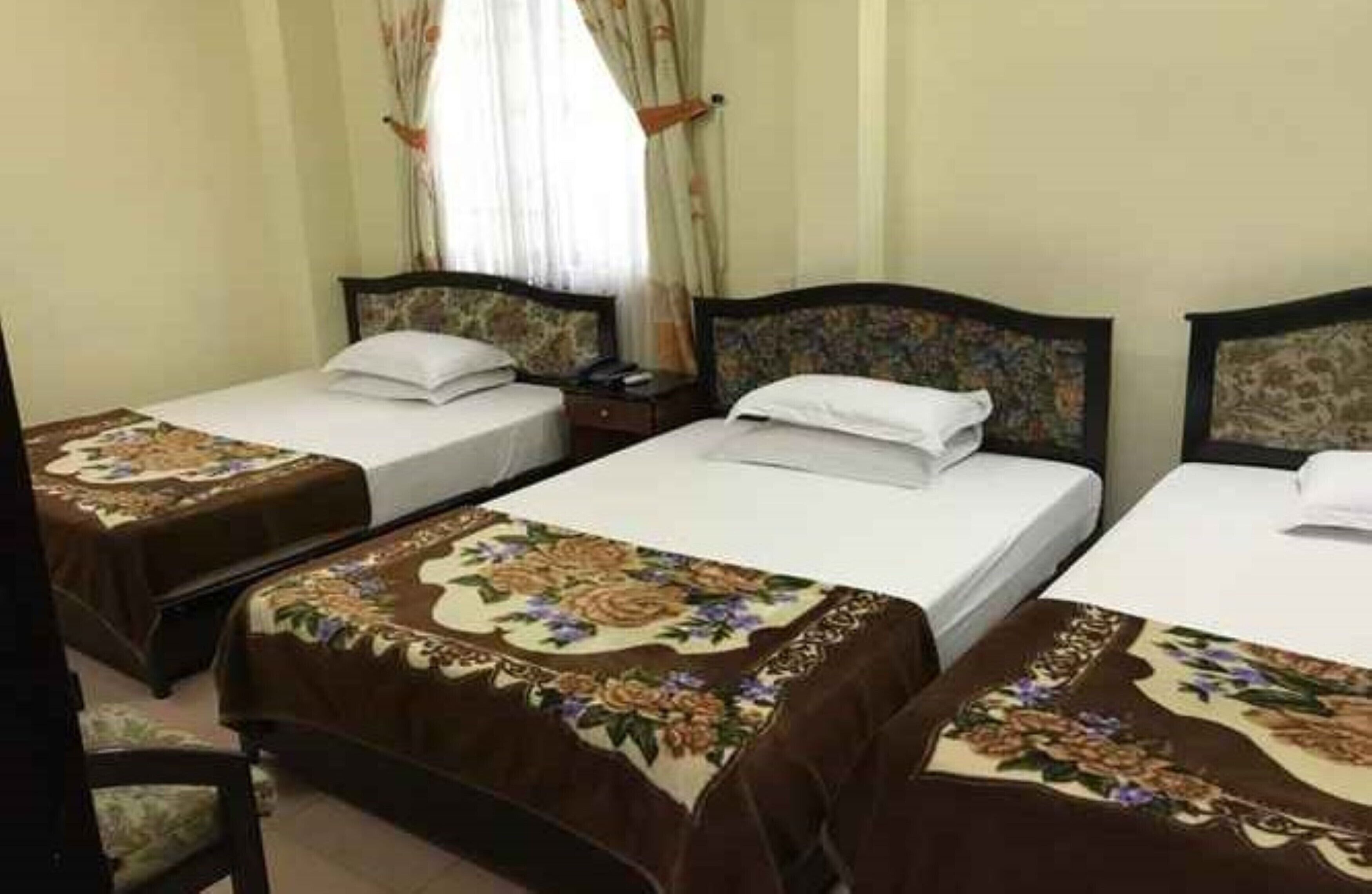 Une chambre d’hôtel avec deux lits simples, chacun agrémenté d’une couvre-lit à motifs floraux et d’une tête de lit assortie. Il y a une table de chevet entre les lits, ainsi qu’une fenêtre avec des rideaux.