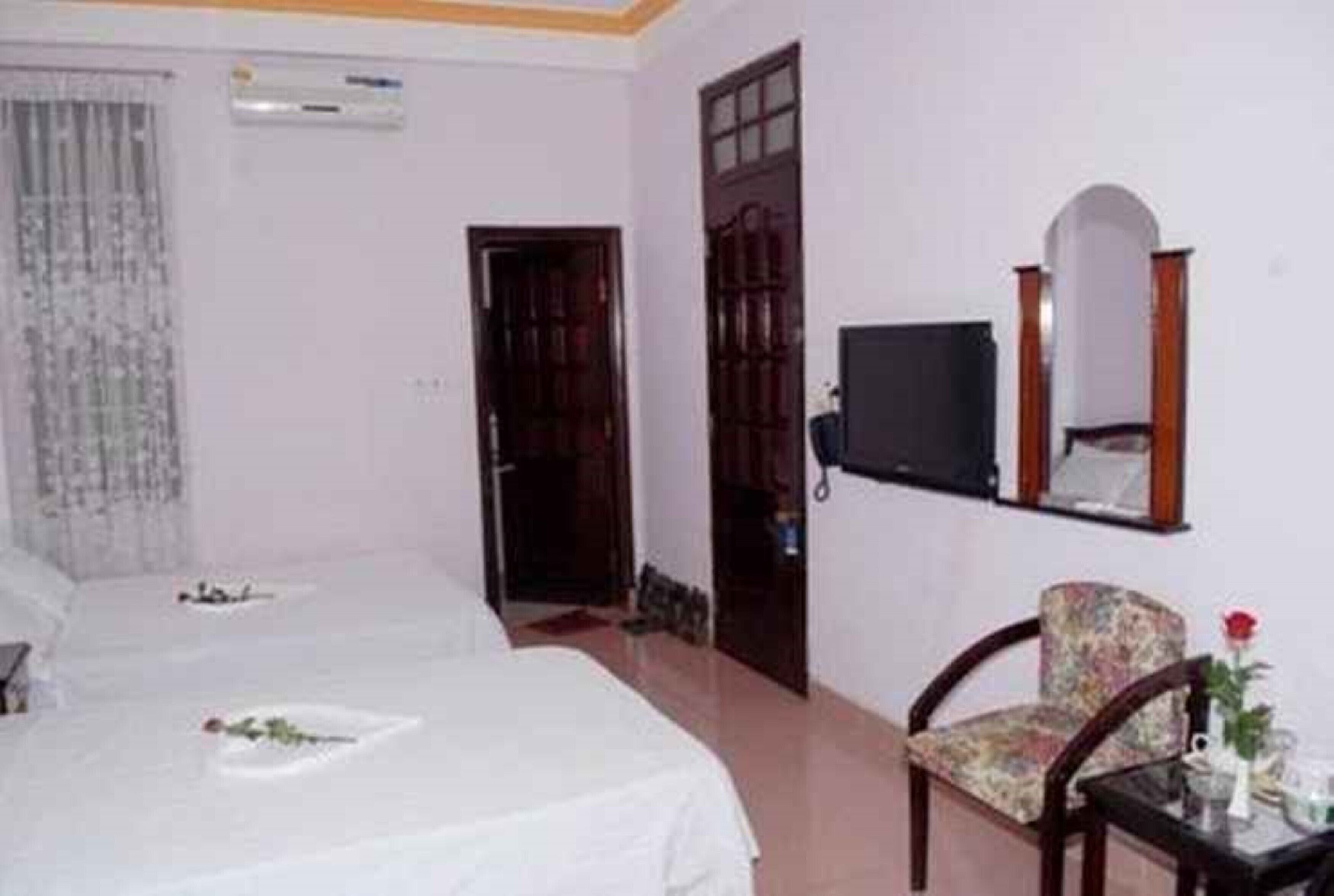 A hotel room with two beds, a television, a chair, and a mirror.